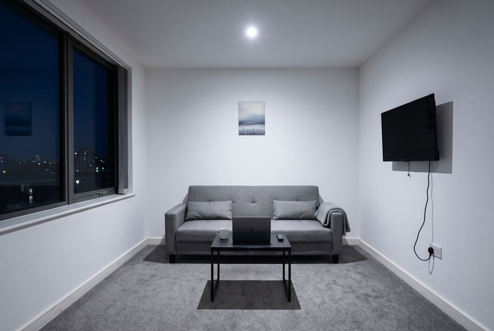 Bare grey living room at night before Decora redesign, lit by a single ceiling downlight